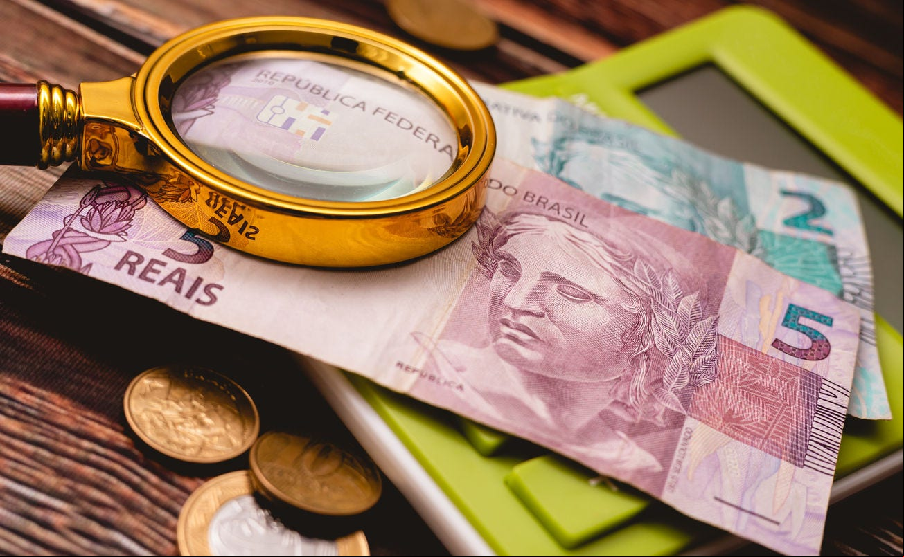 Real currency, Money from Brazil. A Brazilian Real banknotes on a calculator with a magnifying glass in the image composition that are on a wooden table. Concepts of Brazilian economy and finance.